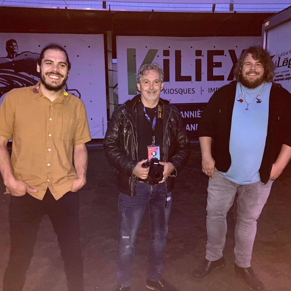 Pierre Dassylva, appareil photo au cou, en coulisses avec deux musiciens